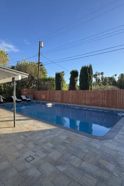 Pools Los Angeles technician using a professional net to remove leaves and surface debris from a blue swimming pool.